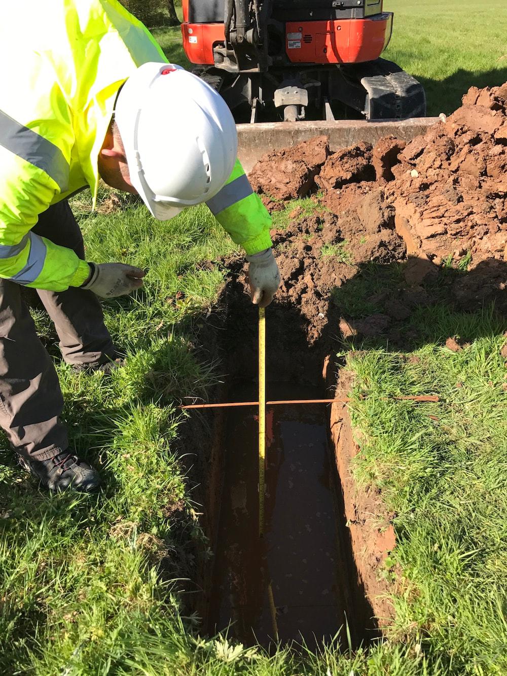 Field technician in PPE measuring depth in a perc test pit